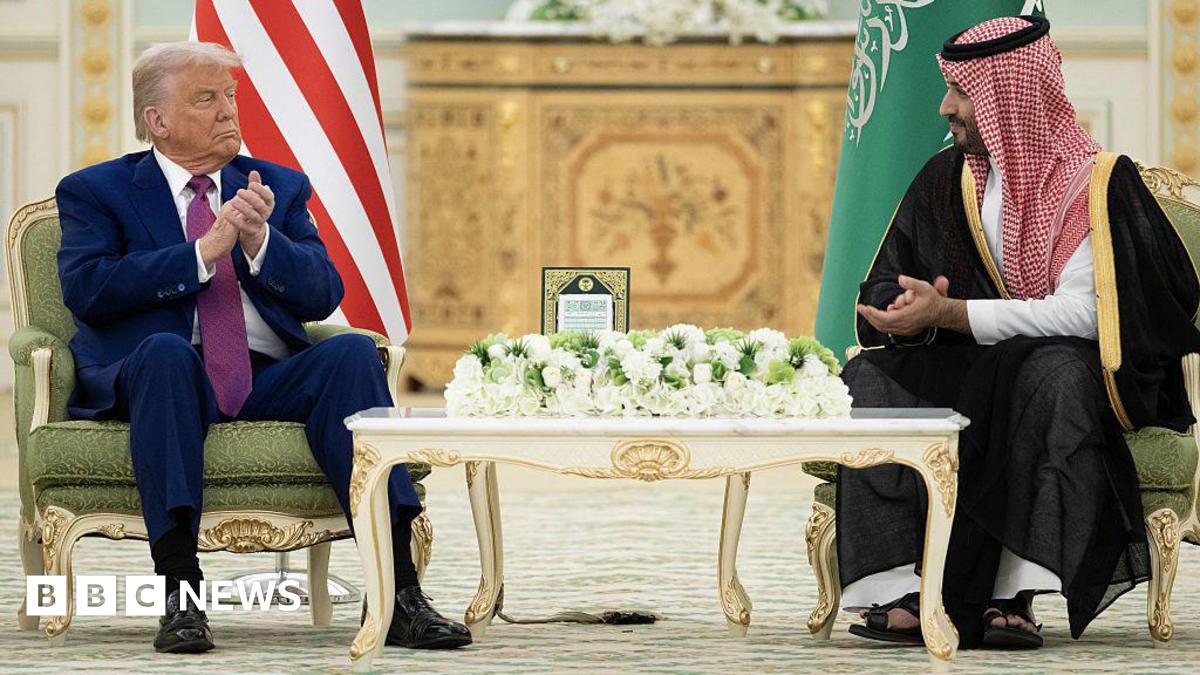 US President Donald Trump and Saudi Crown Prince Mohammed bin Salman sit in green gilded armchairs, the flags of their countries behind them, as they applaud and look at one another. Trump wears a blue suit, white shirt and purple tie while bin Salman wears a black dress and red and white headscarf.