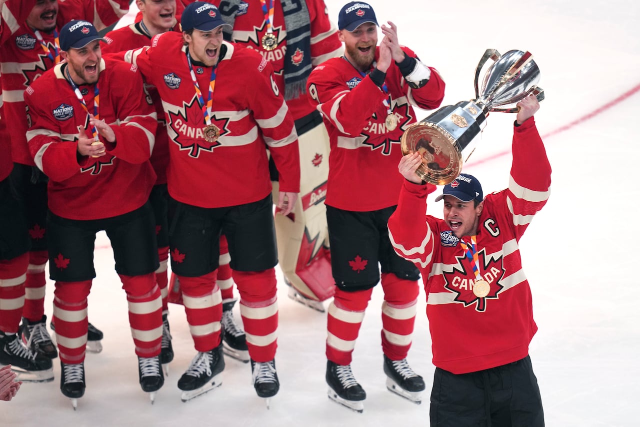 A hockey player lifts a trophy as the team celebrates beside him.