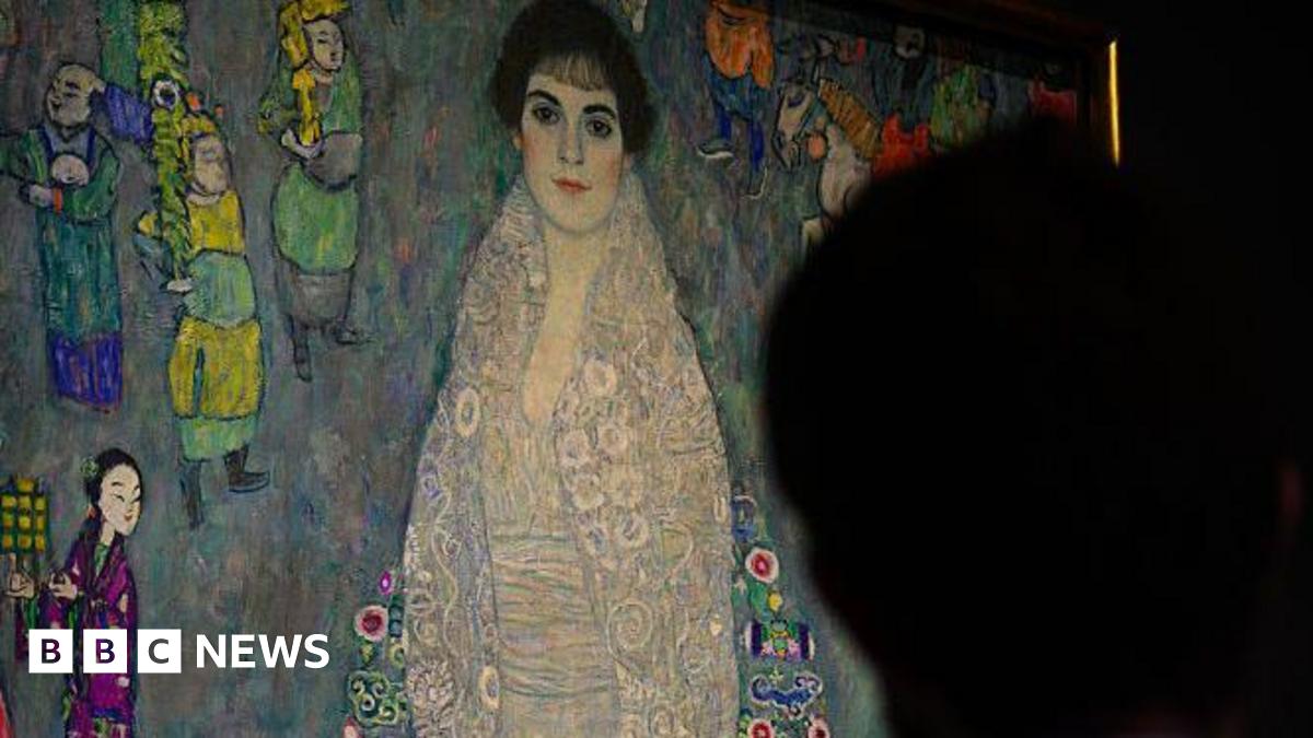 A man stands in front of a full-length Art Nouveau portrait of a woman.