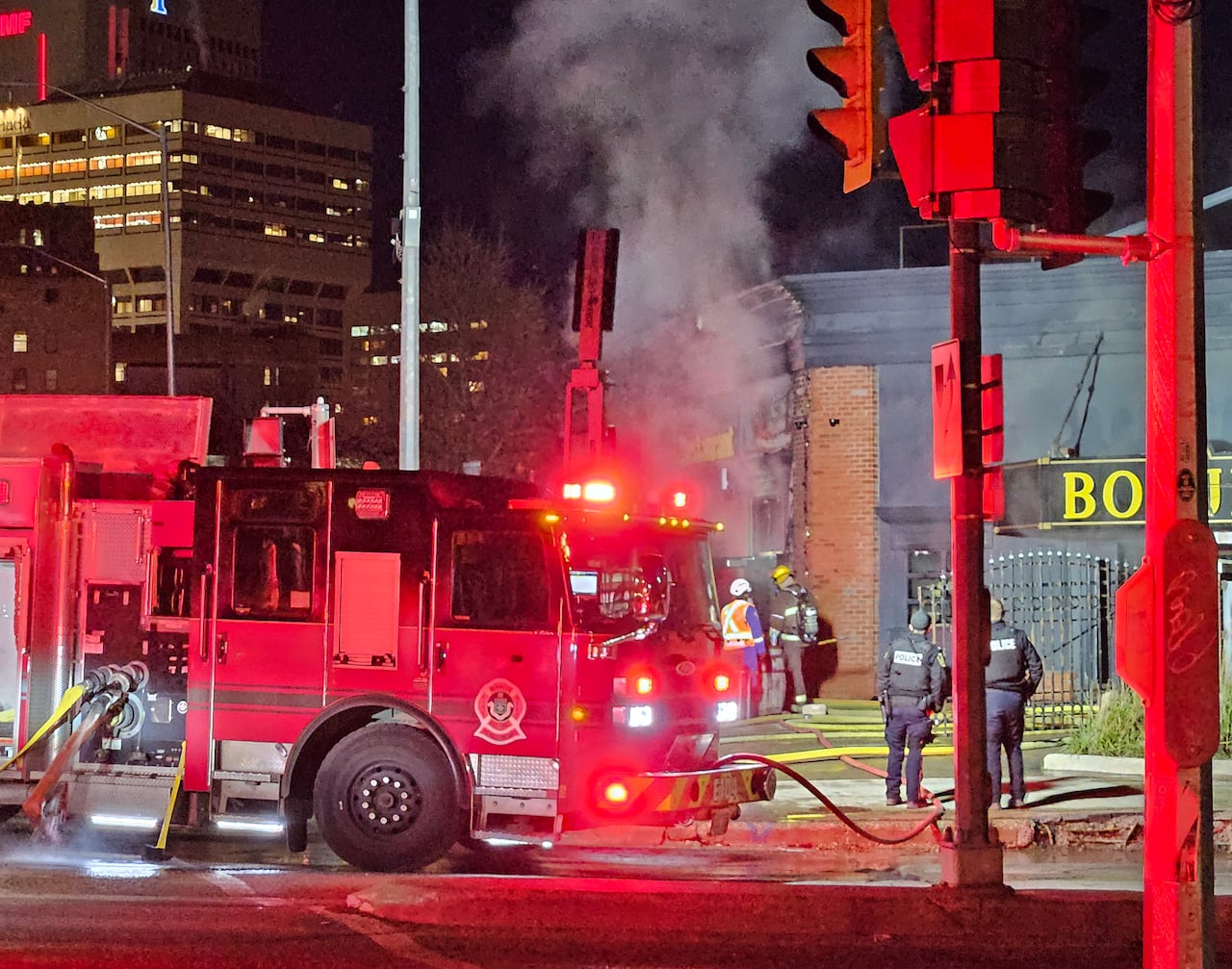 A fire truck is in the foreground while smoke pours from a building in the background.