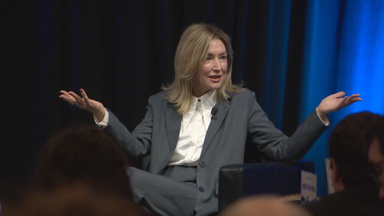 a formally dressed woman sits on a chair in front of an audience