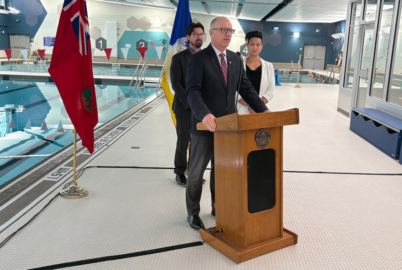 Three people stand and talk at a podium inside a pool area