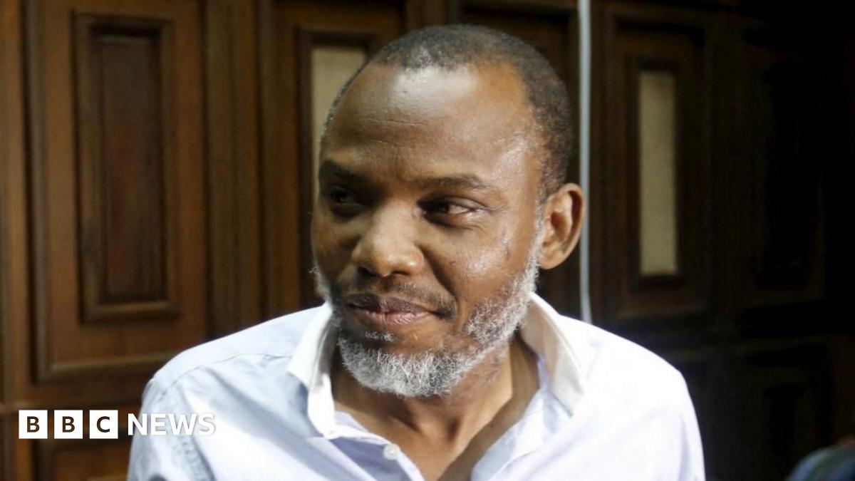 A head-and-shoulders shot of Nnamdi Kanu, in an open-necked white shirt, looking to the left of the picture. He is in a wood-panelled court room.