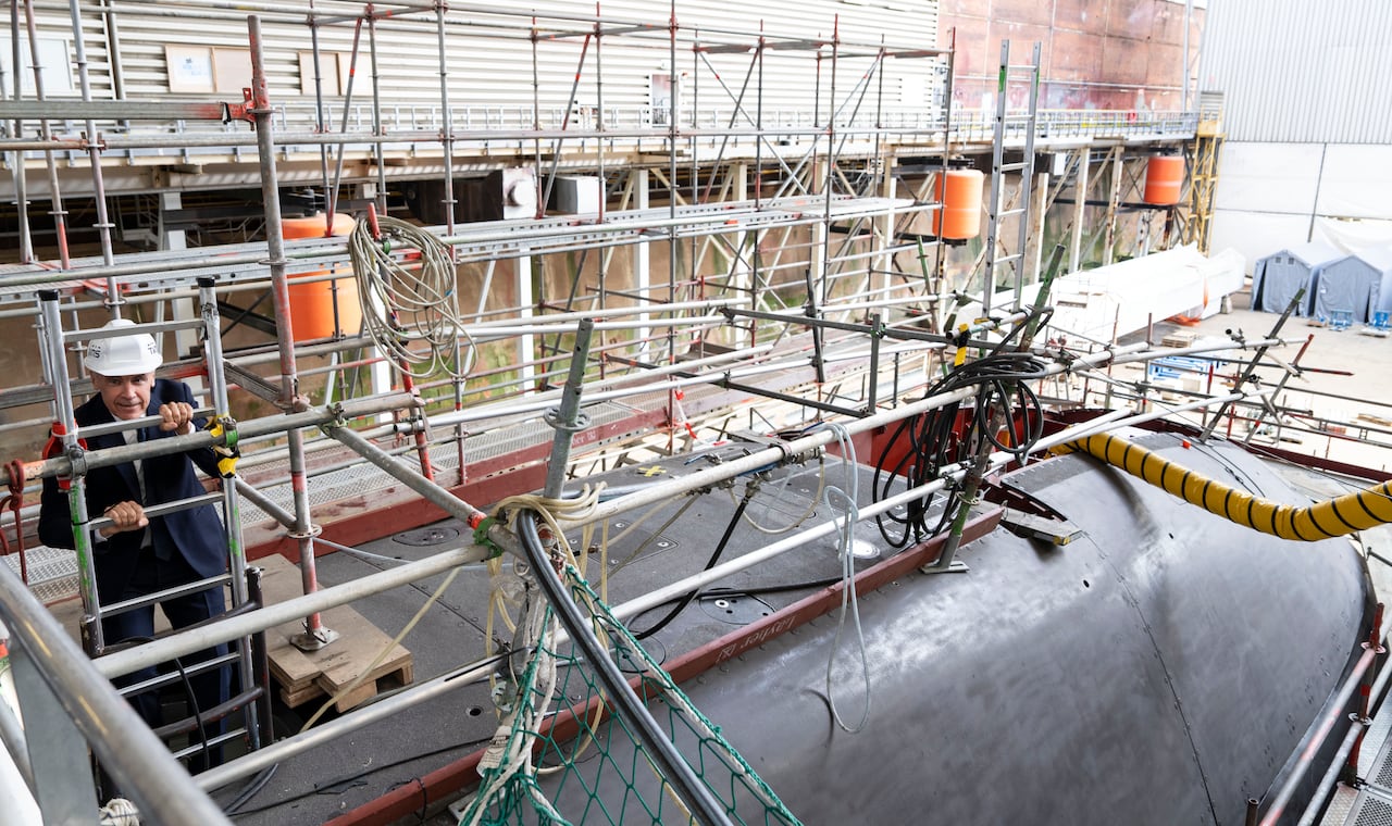 A man in a hard hat climbs on a ladder out of a submarine.