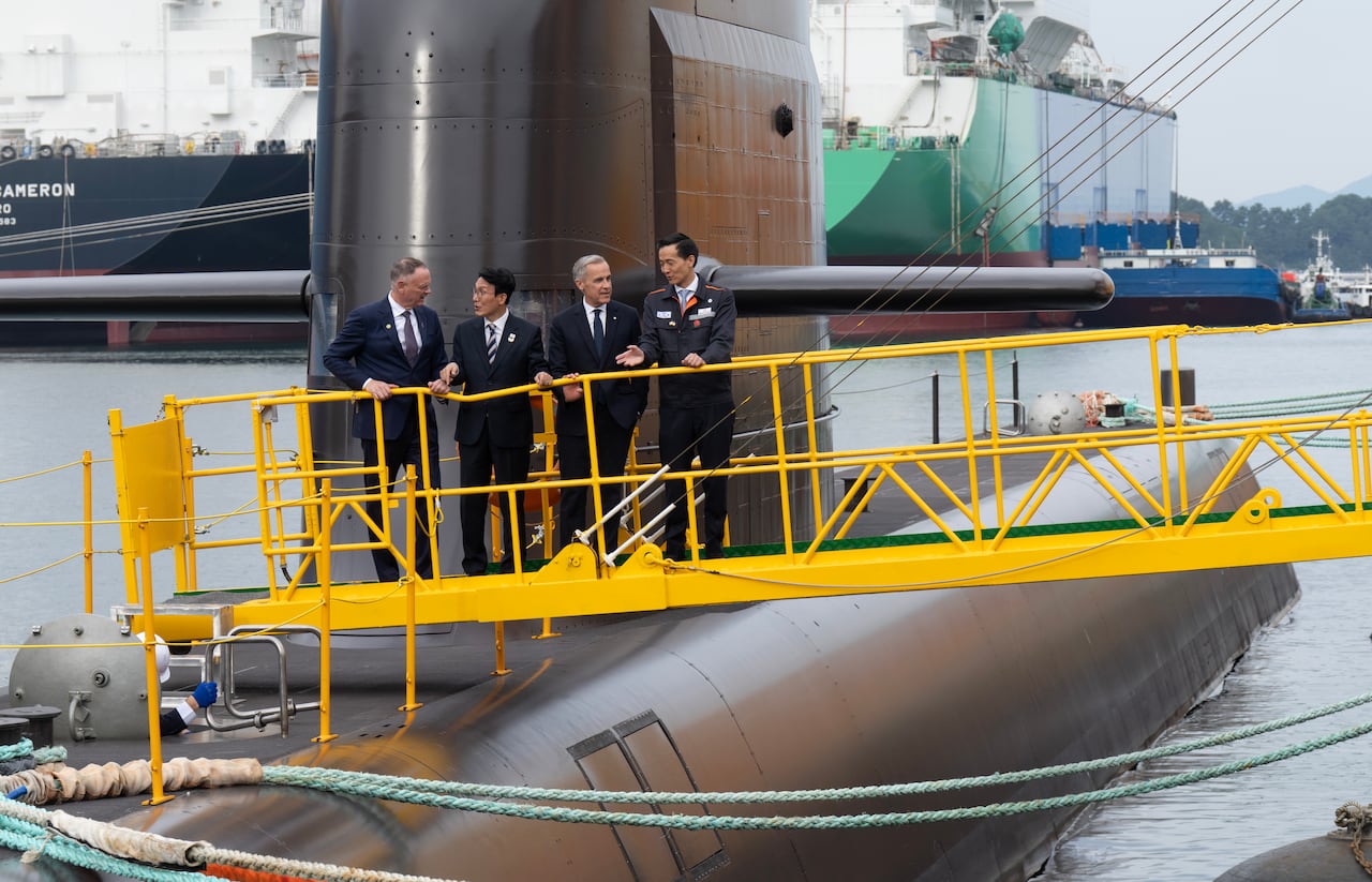 Four men in suits standing on a bridge above a submarine.