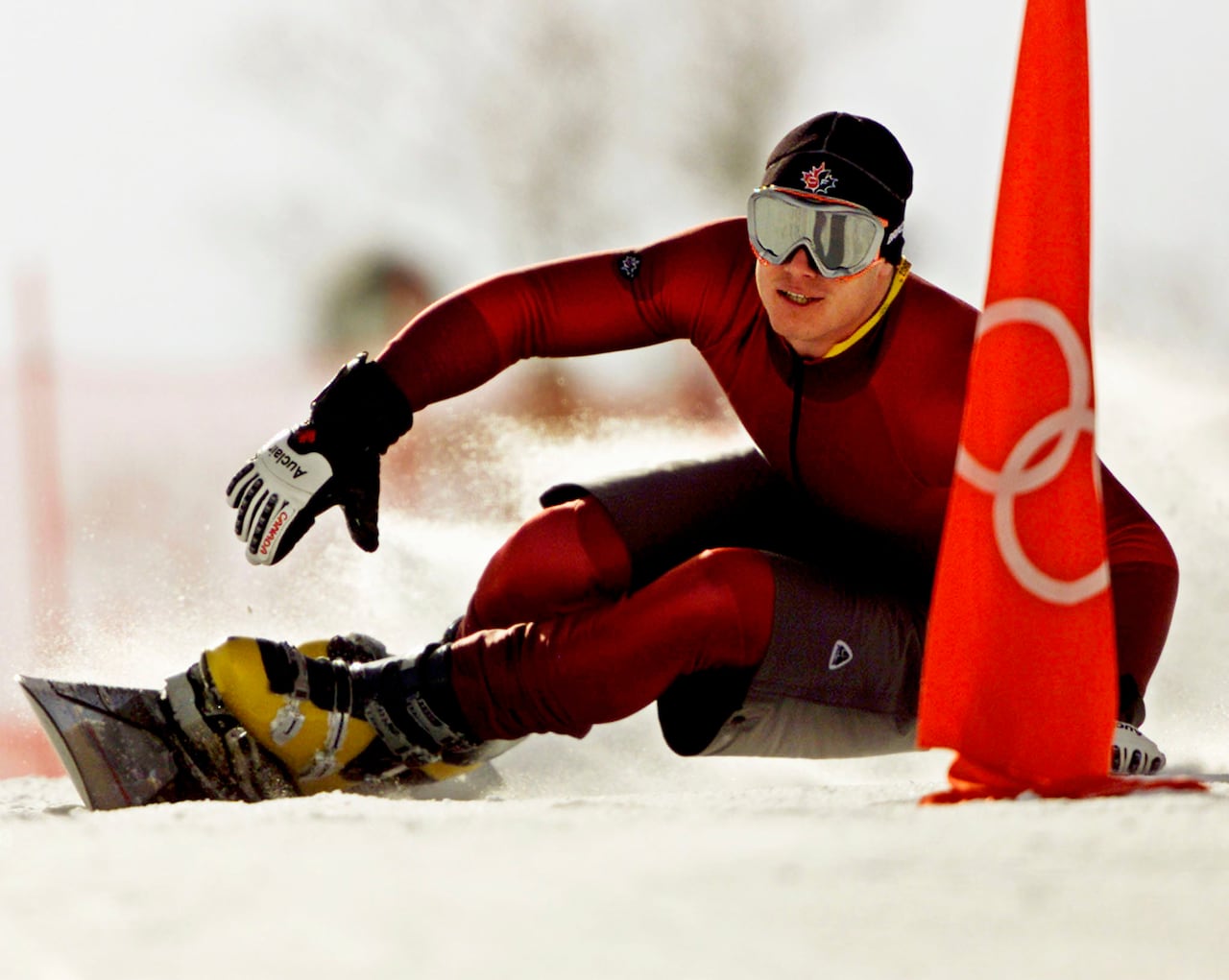 Man in red ski suit and dark goggles snowboards down a course on a hill