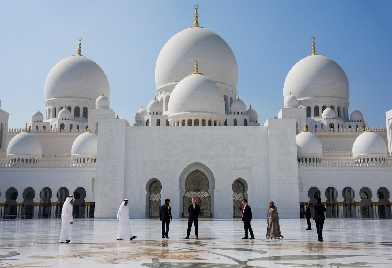 A group of people stand in front of several domes of a mosque on a sunny day.