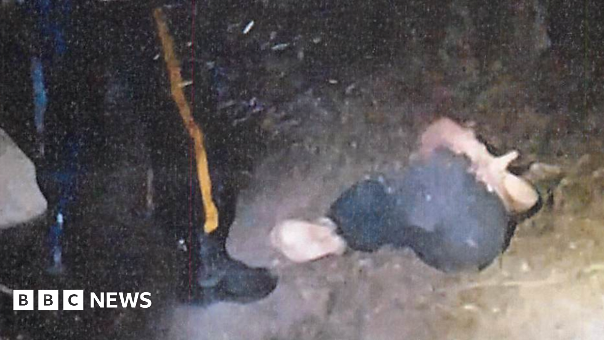 A grainy photo shows a dirt ground with a woman tied up and lying in the fetal position. The leg of a person apparently in uniform is next to her and it appears to be dark outside.