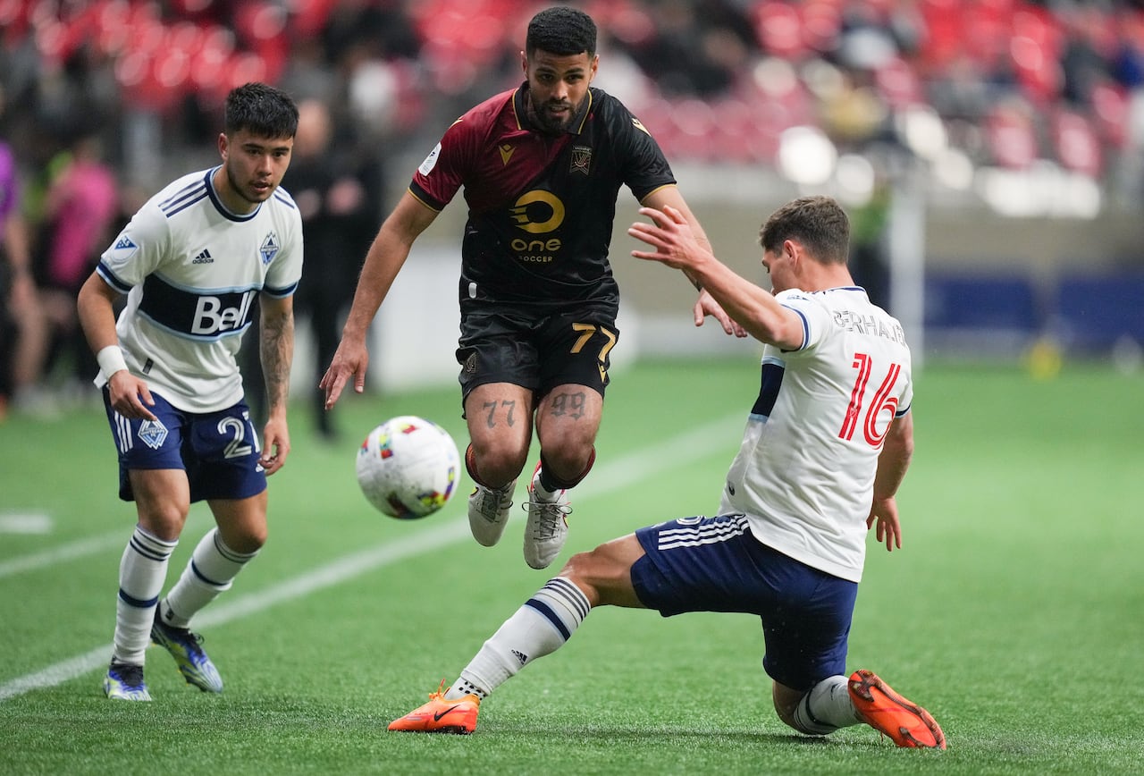 A soccer player on a field jumps with two other players on either side of him.