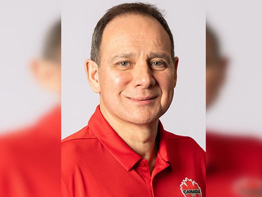 A man in a red shirt smiles in a portrait image