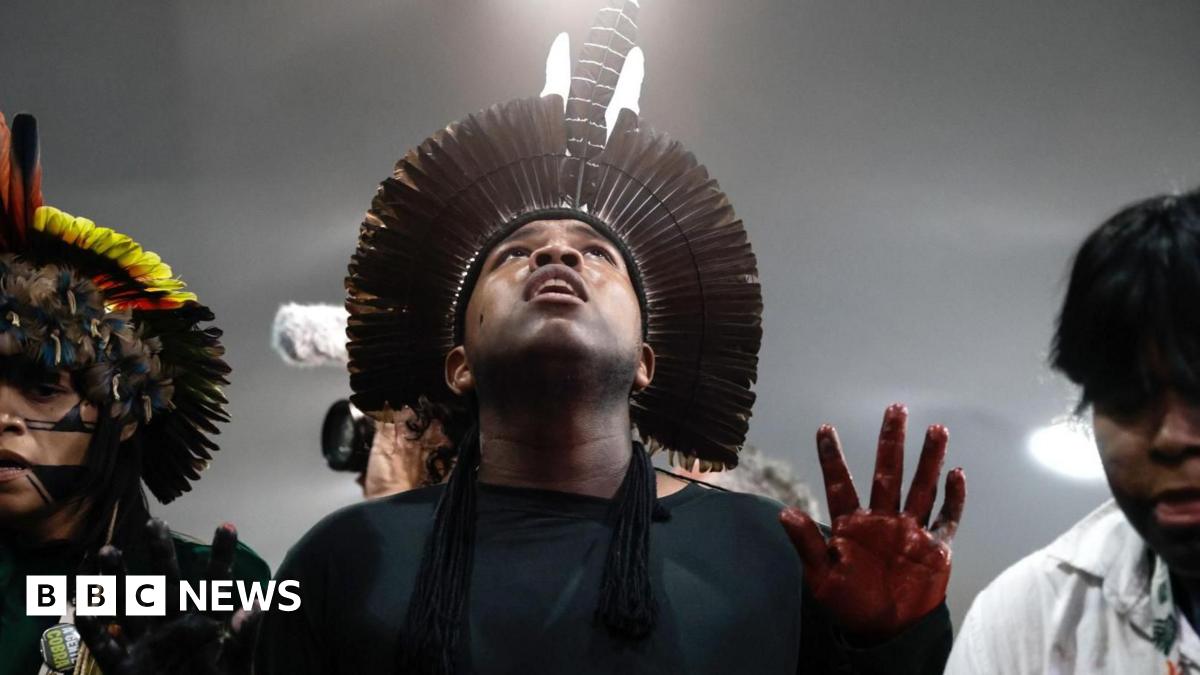 Paul Costelloe has receding grey hair. He is wearing a bright pink, blue and green scarf and a blue jacket.