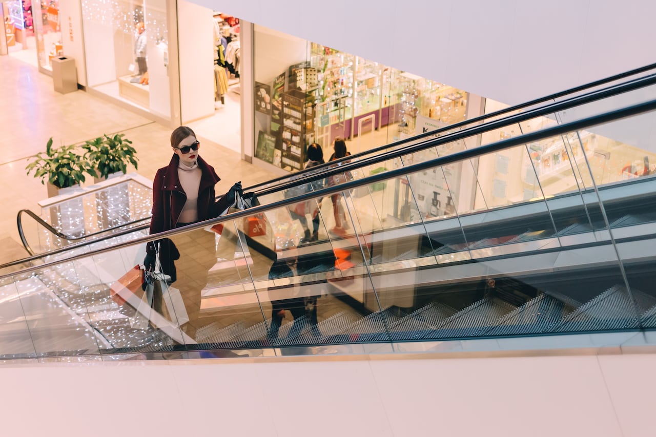 A woman in sunglasses going up an escalator at a shopping mall. 