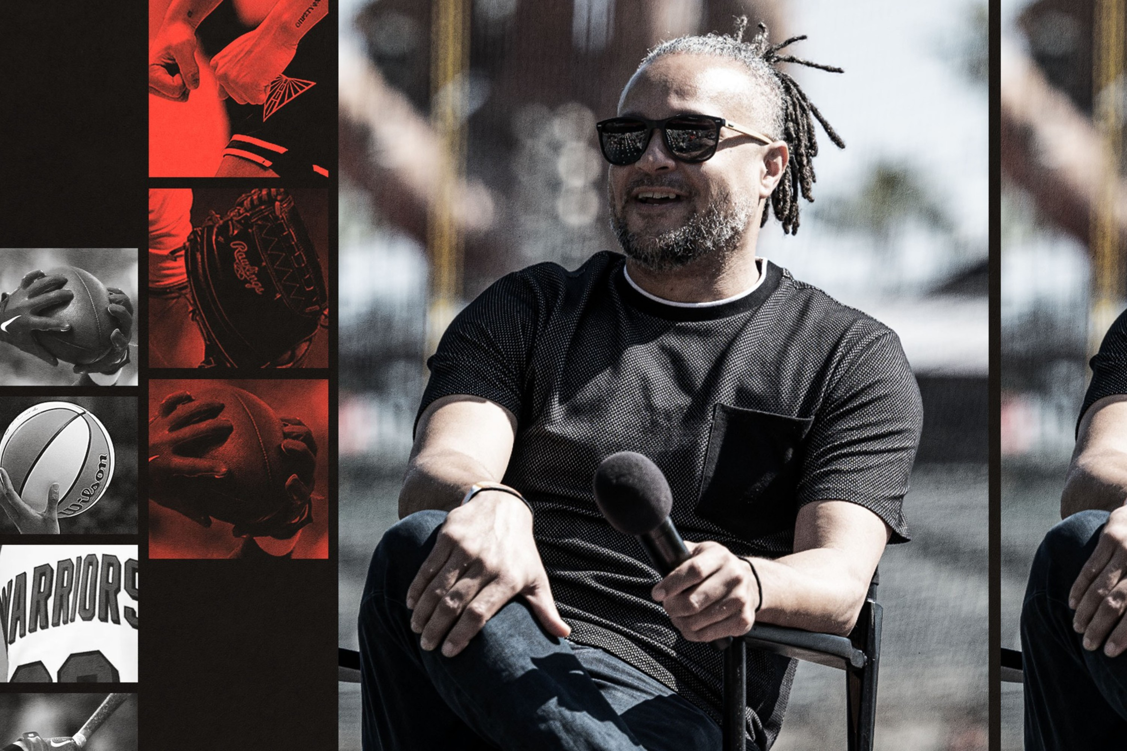 A man with dreadlocks and sunglasses sits casually holding a microphone, wearing a black shirt and jeans, with a blurred outdoor background.