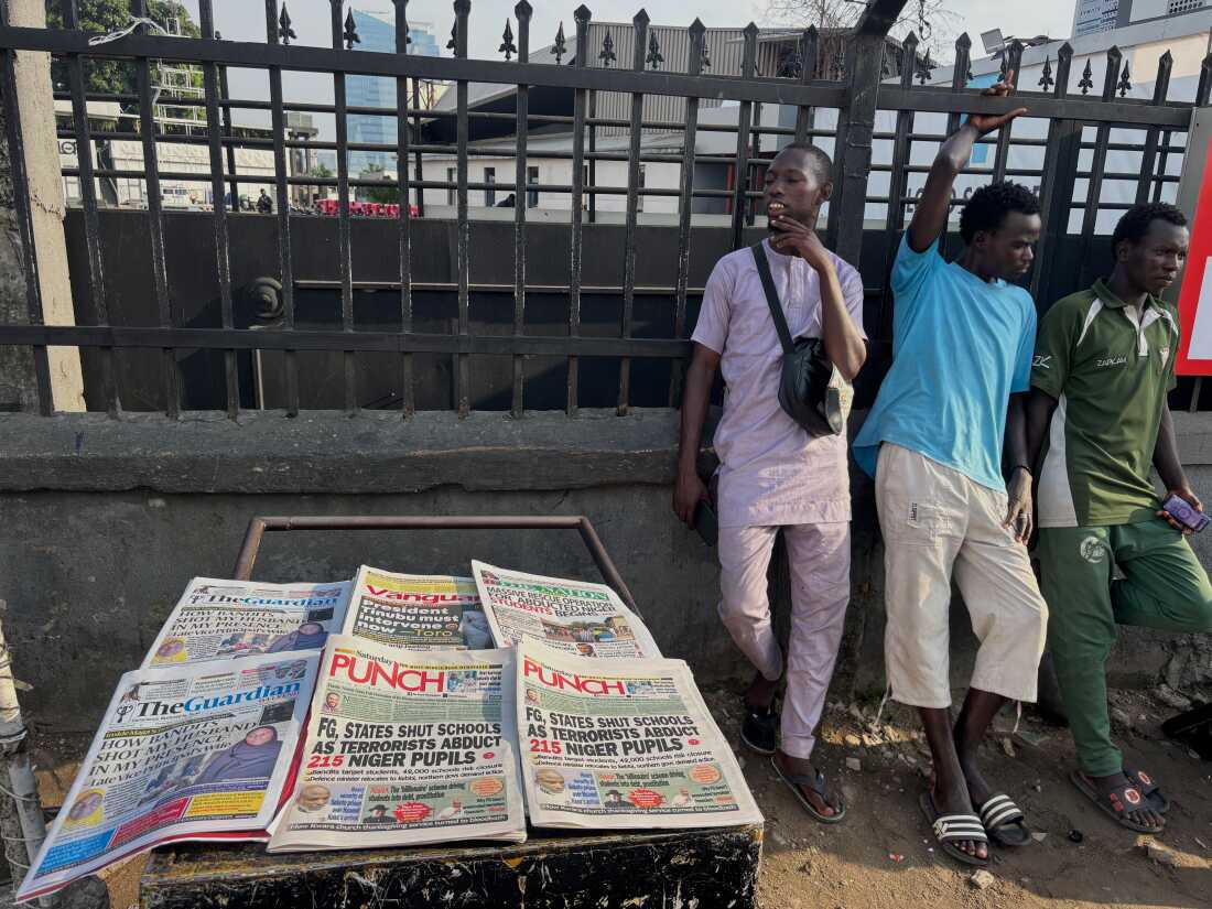 People stand near a display local newspapers on the street of Lagos with headlines on gunmen abducting schoolchildren and staff of the St. Mary's Catholic Primary and Secondary School in Papiri community in Nigeria, Saturday, Nov. 22, 2025.