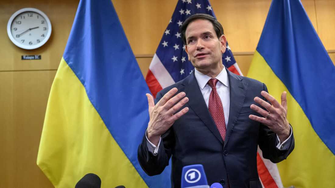 U.S. Secretary of State Marco Rubio talks during a press conference. Behind him are two Ukrainian flags and an American flag.