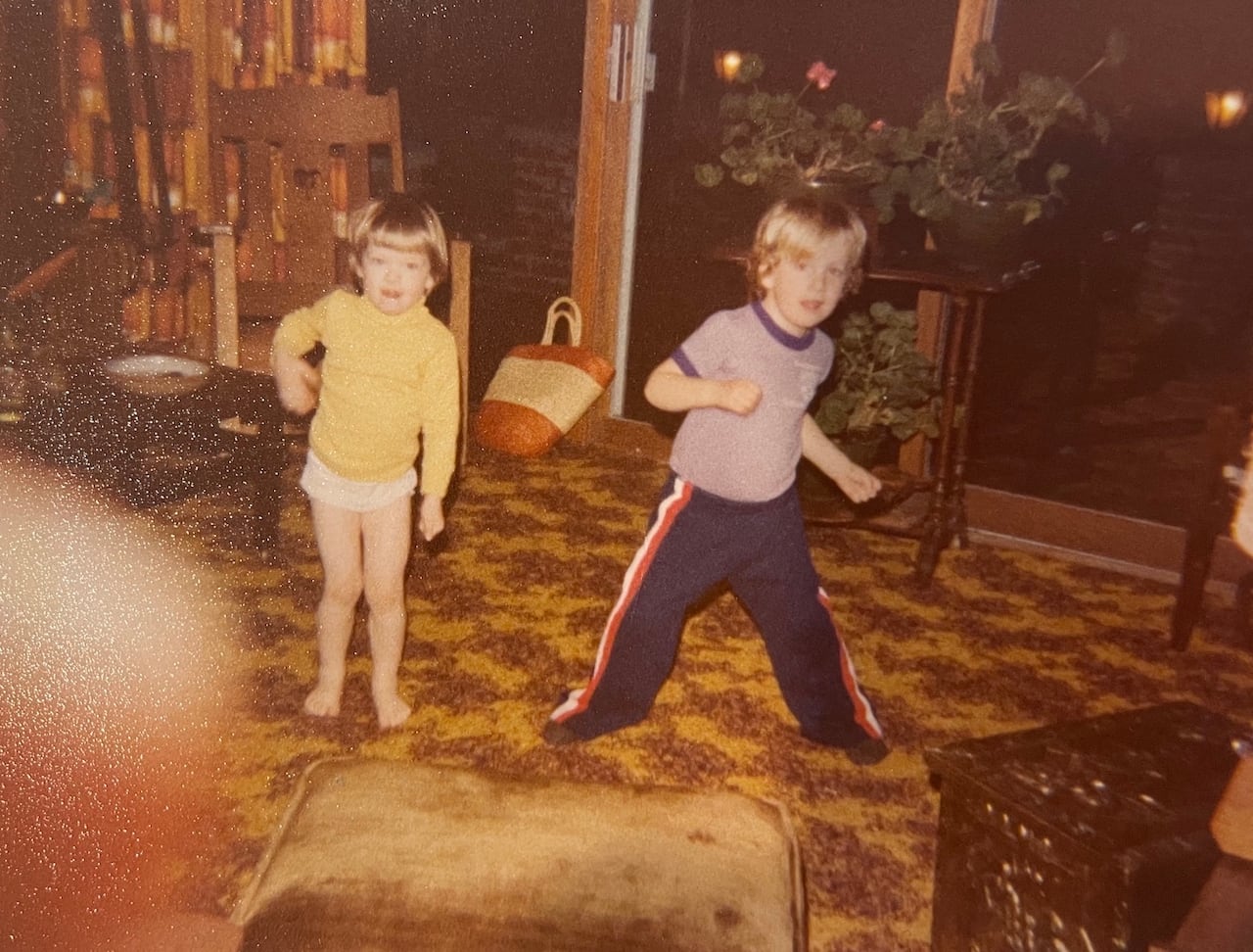 An old photo of two blond kids on a brown rug