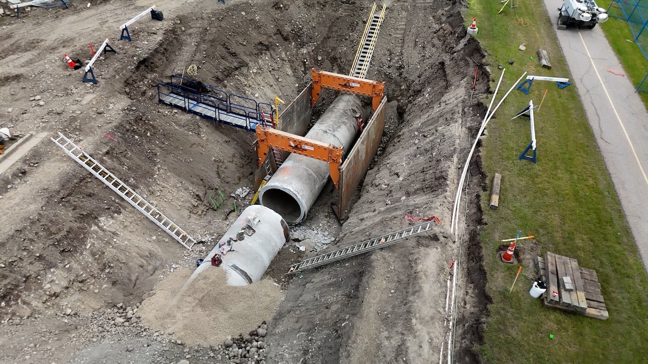 a large open excavation site with heavy duty construction equipment and workers working on a large exposed underground pipe.