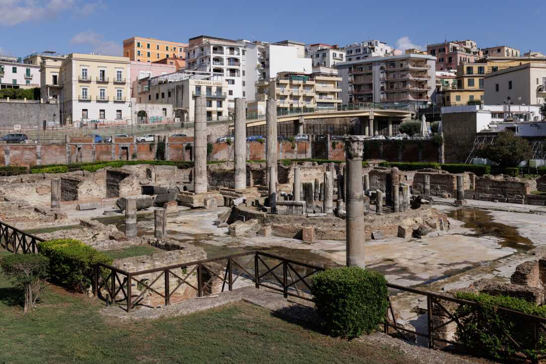 Ancient Roman ruins are seen surrounded by modern buildings.