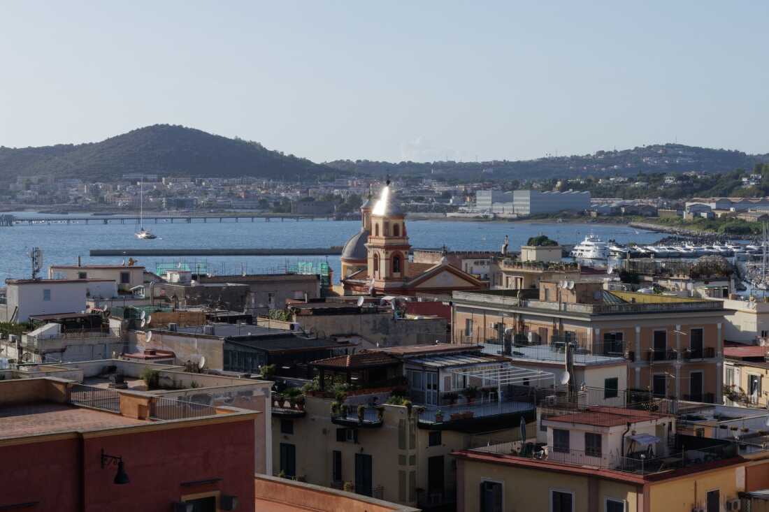 A view of Pozzuoli: in the foreground, the Church of Santa Maria delle Grazie; in the background, the waterfront, the marinas, and the hills of the Campi Flegrei, with the sea surrounding the city.