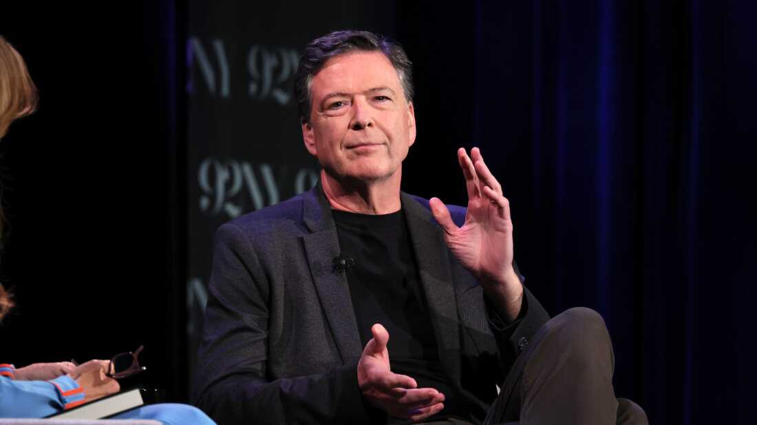 James Comey speaks onstage during Former FBI Director James Comey In Conversation With MSNBC's Nicolle Wallace in 2023. He sits in a chair and wears an all black outfit. 