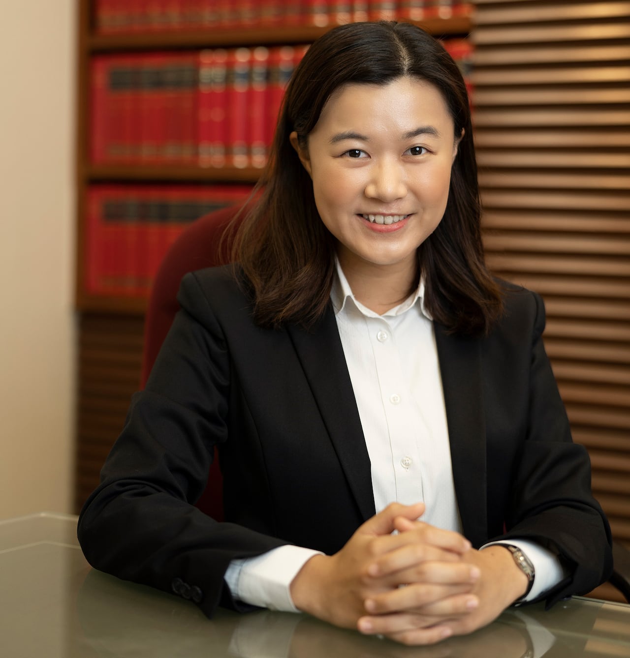 A woman sits at a table with full bookshelves visible in the background.