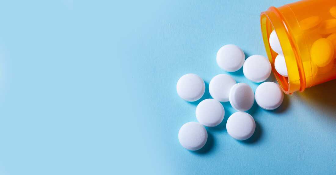 White round pills in orange bottle on blue background banner close up with copy space