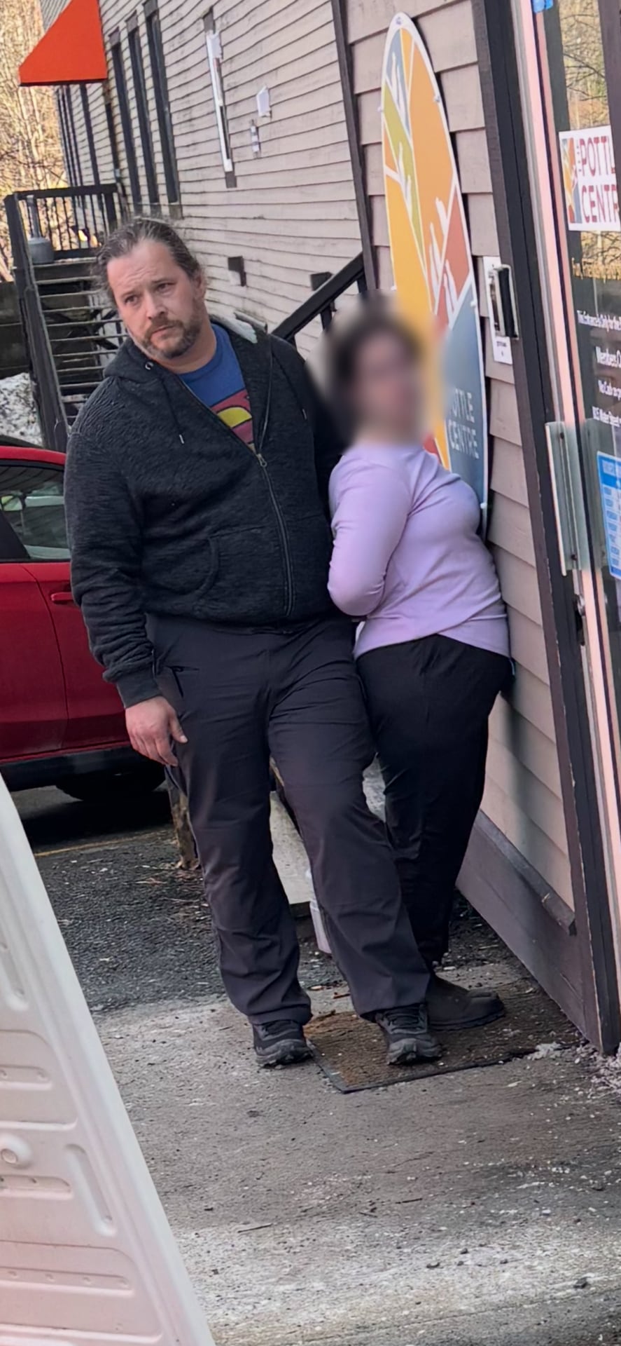 A man holds his body against a woman as she is back on, facing an exterior wall. 