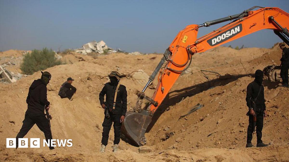 Masked and armed militants guard a digger at an excavation site.