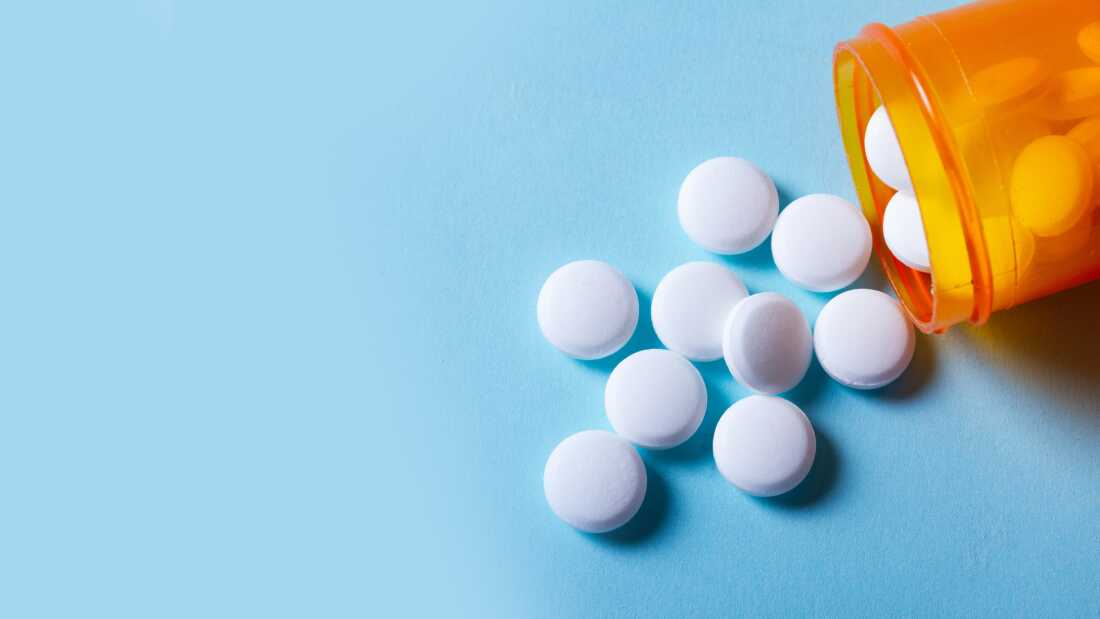 White round pills in orange bottle on blue background banner close up with copy space