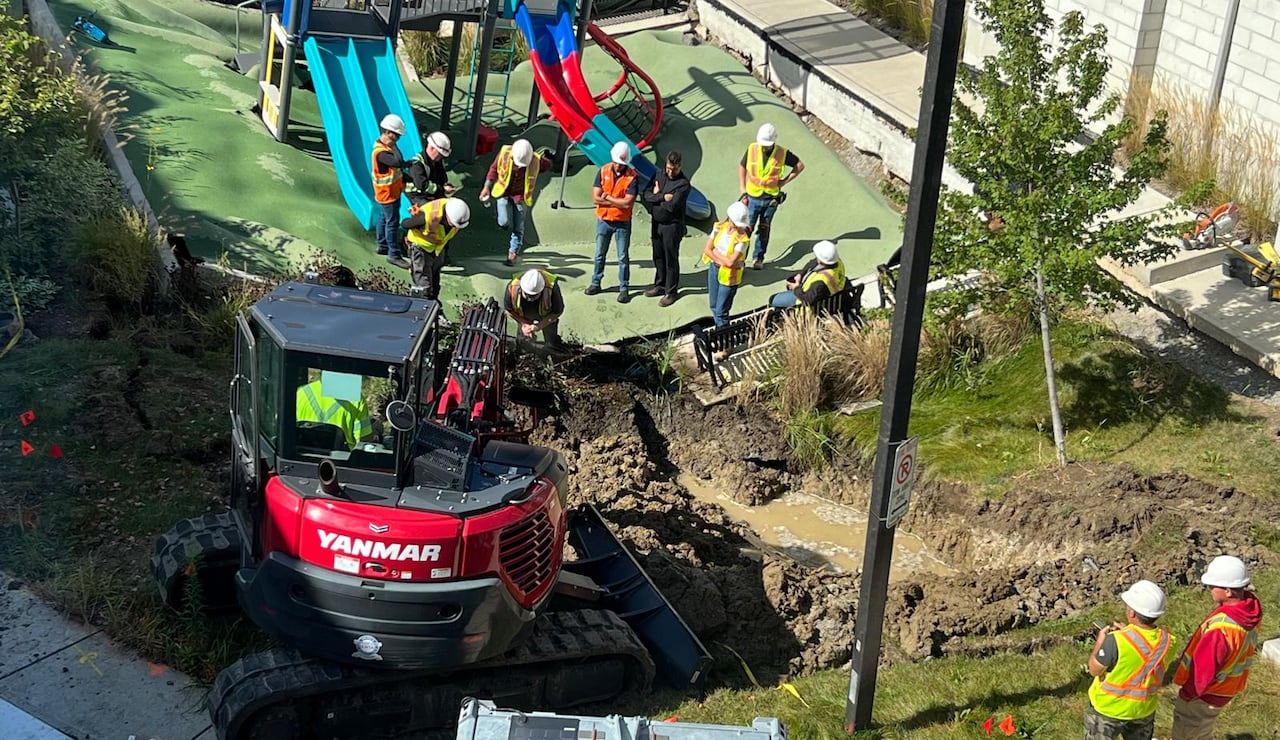 View looking down on the collapsed playground. About a dozen people are standing, most wearing high visibility vests, looking at the damage. 