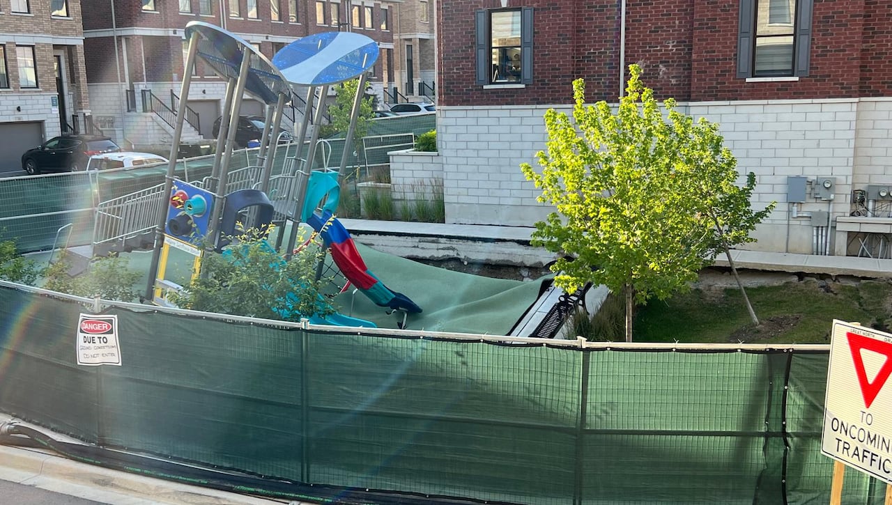 Playrgound equipment and trees tilted at an angle, with the ground sinking beneath it. The are is fenced off. 