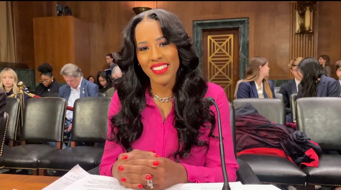 A woman sits at a table with her hands folded in front of her
