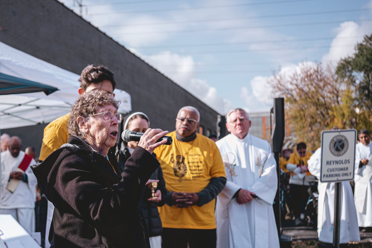 A woman addresses an outdoor crowd while others, in religious garb, look on. 