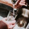 Close-up of a man turning a tap on in a kitchen, pouring himself a glass of water into a transparent drinking glass.