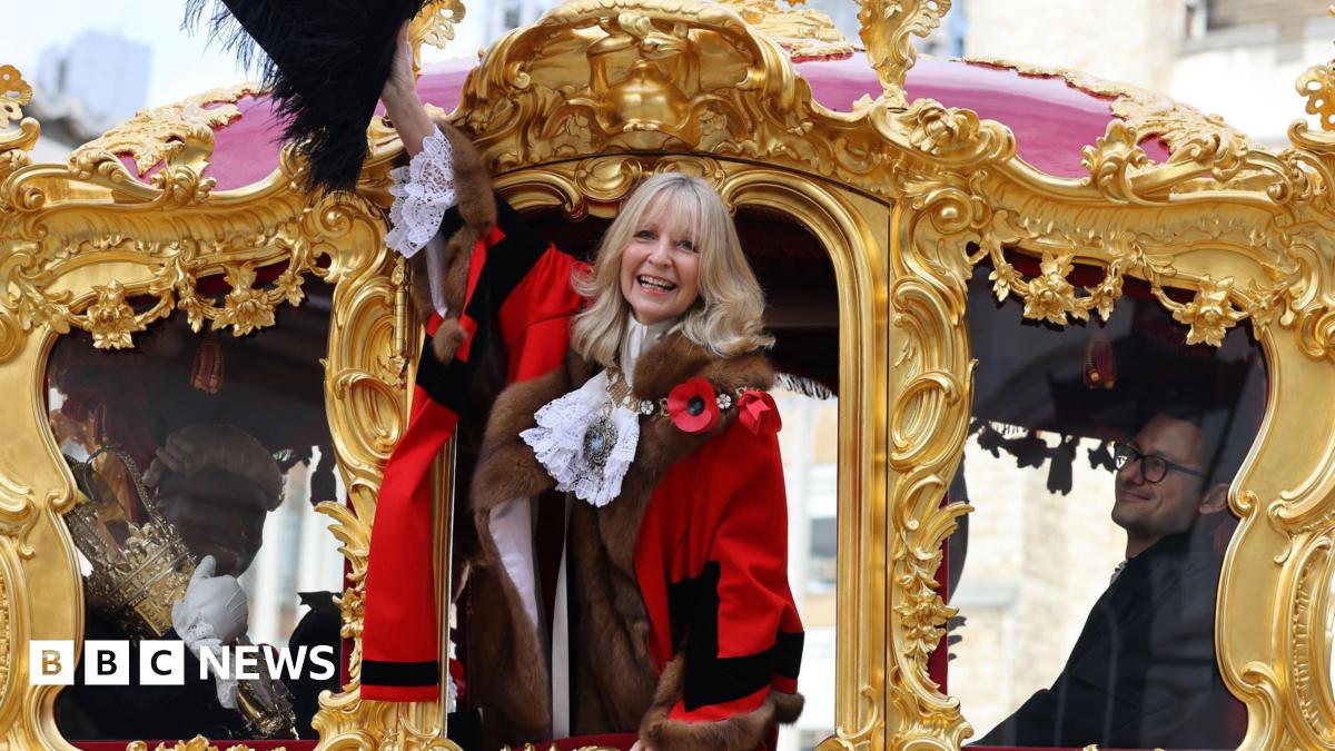 A woman in municipal robes waves from the door of an 18th century golden coach.