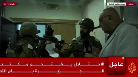 Reuters Screengrab of Al Jazeera TV broadcast showing Israeli soldiers handing over orders to bureau chief Walid al-Omari, at Al Jazeera's office in Ramallah, in the occupied West Bank (22 September 2024)