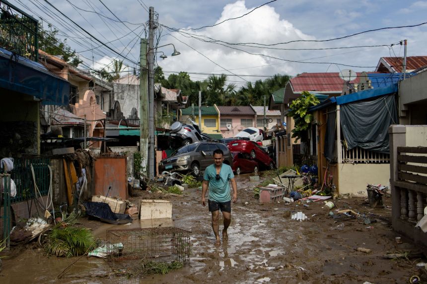 A man walks along a muddy street where cars piled up after being swept away in floods brought by Typhoon Kalmaegi pile up in Bacayan, Cebu City, Philippines, on November 5, 2025.