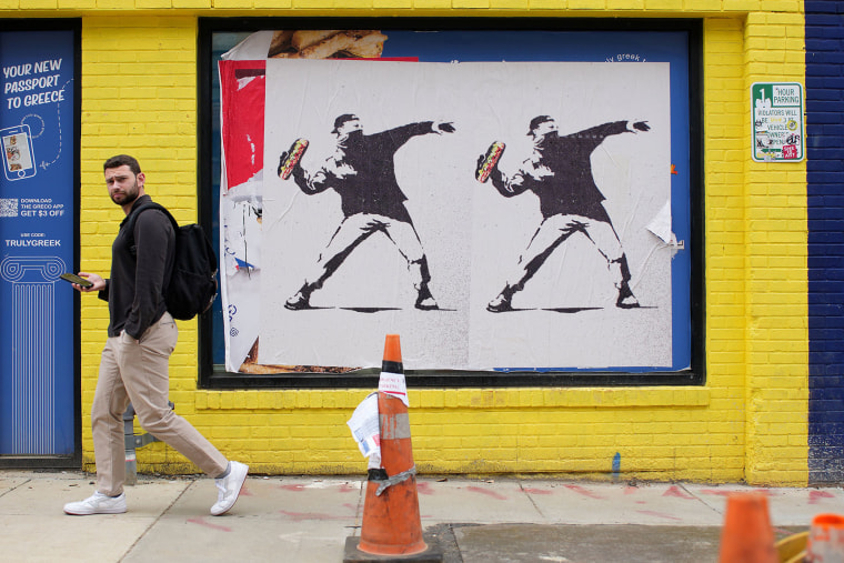 A person walks past Banksy-style posters of a protester throwing a sandwich on Aug. 21, 2025.