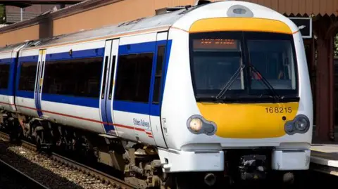 Getty Images A Chiltern Railway Train stands at the platform at Birmingham Moor Street Station. The train has blue and white sides with a red line and the company logo. The front of the train is yellow.