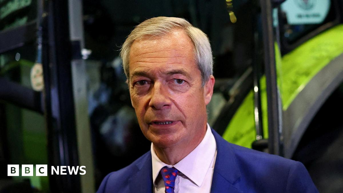 Nigel Farage wearing a serious expression standing in front of a mechanical digger
