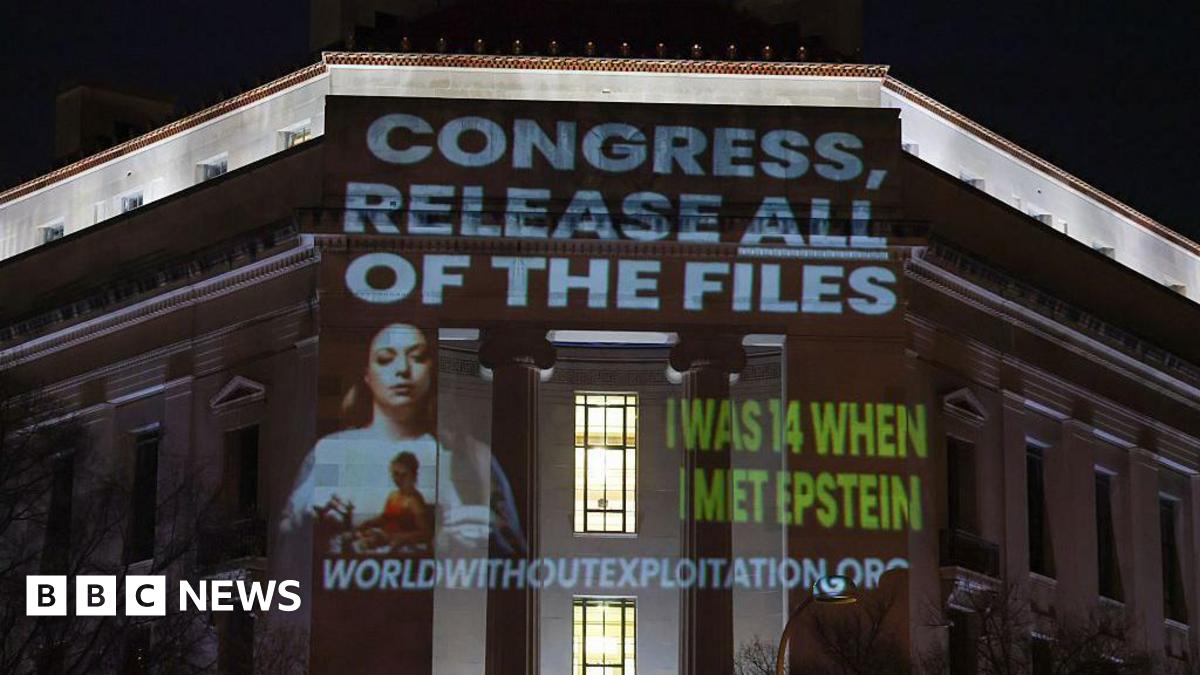 Wording is projected at nighttime onto a building that includes the phrase "Congress, release all files" in capital letters and a white font above a photo of a woman with long brown hair. The words "I was 14 when I met Epstein" are also seen in all capital letters and a green font