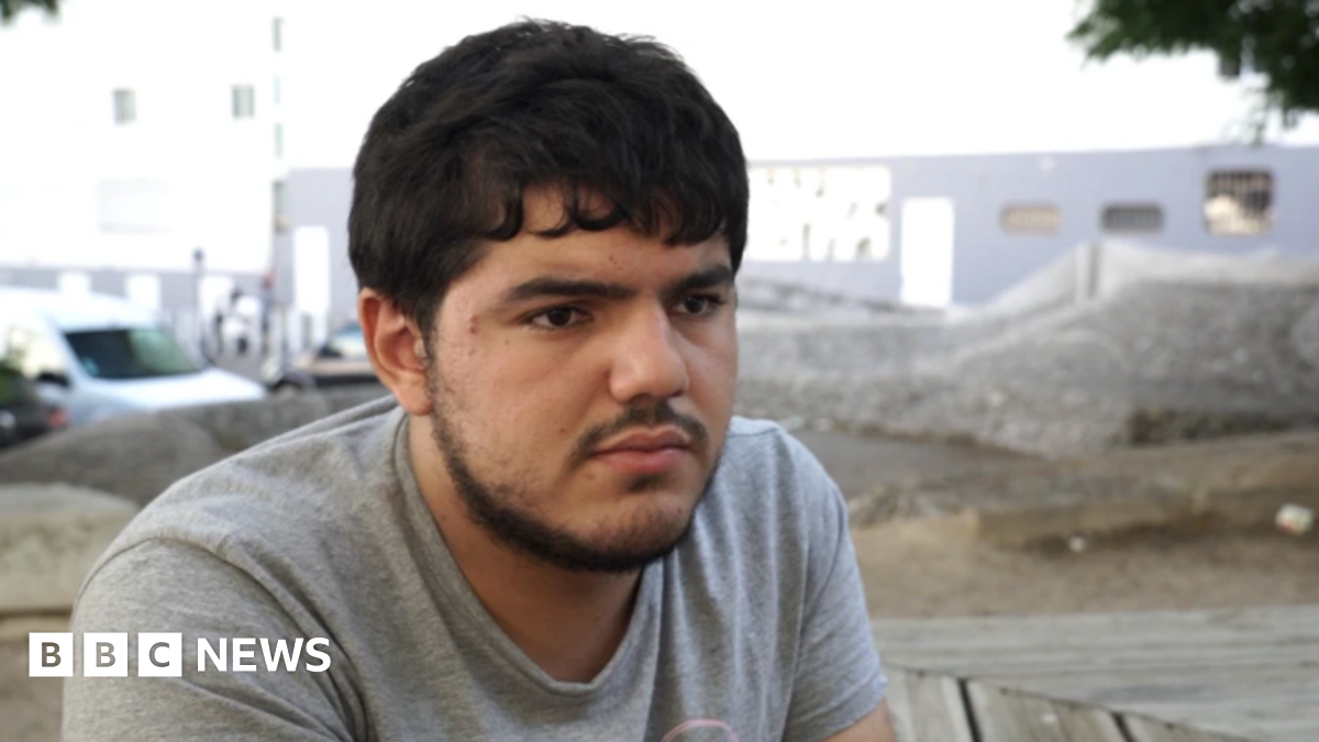 A young man with a beard wears a grey T-shirt and stares out with a backdrop of Marseille
