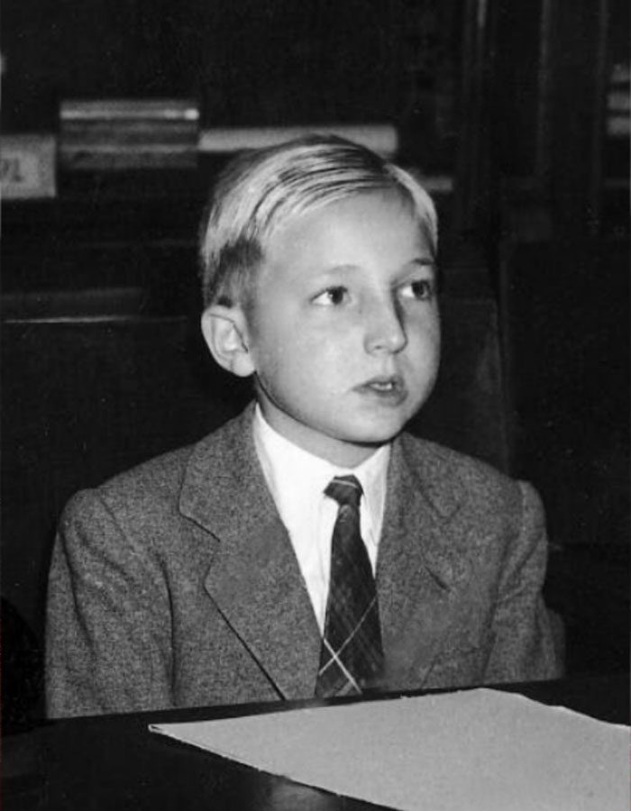 Young boy in a suit and tie, captured in a black and white photo related to former King Juan Carlos and his brother.