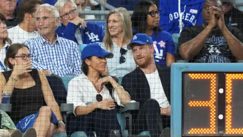 Reuters Meghan Markle and Prince Harry wear blue Dodgers baseball caps while seated in the front row during the third inning between the Toronto Blue Jays and the Los Angeles Dodgers during Game 4 of the 2025 MLB World Series at Dodger Stadium. 