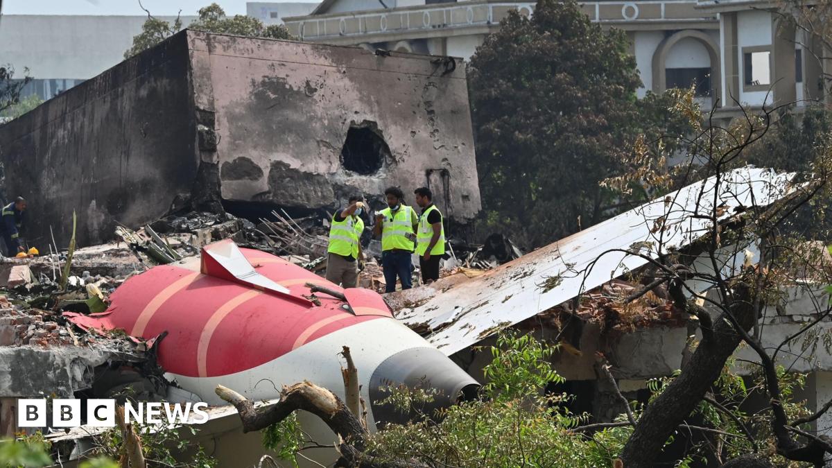 The aftermath of the Air India crash showing a part of the plane crashed in the ground. Three men in high-vis jackets inspect the sight. Taken on 15th June 2025.