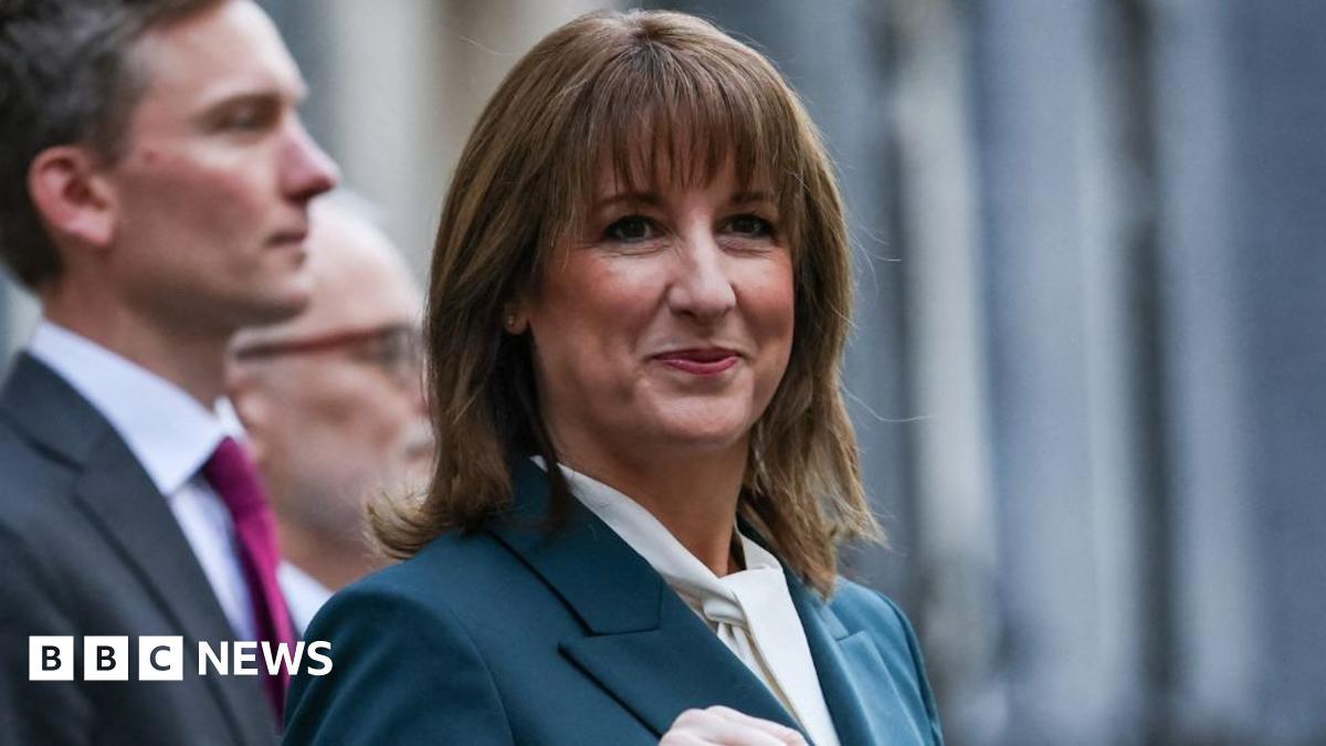 Shona Robison, who has blonde hair tied back, speaks at the foot of a set of stone stairs. She is wearing a dark top with red polka dots and is visible from the shoulders up.