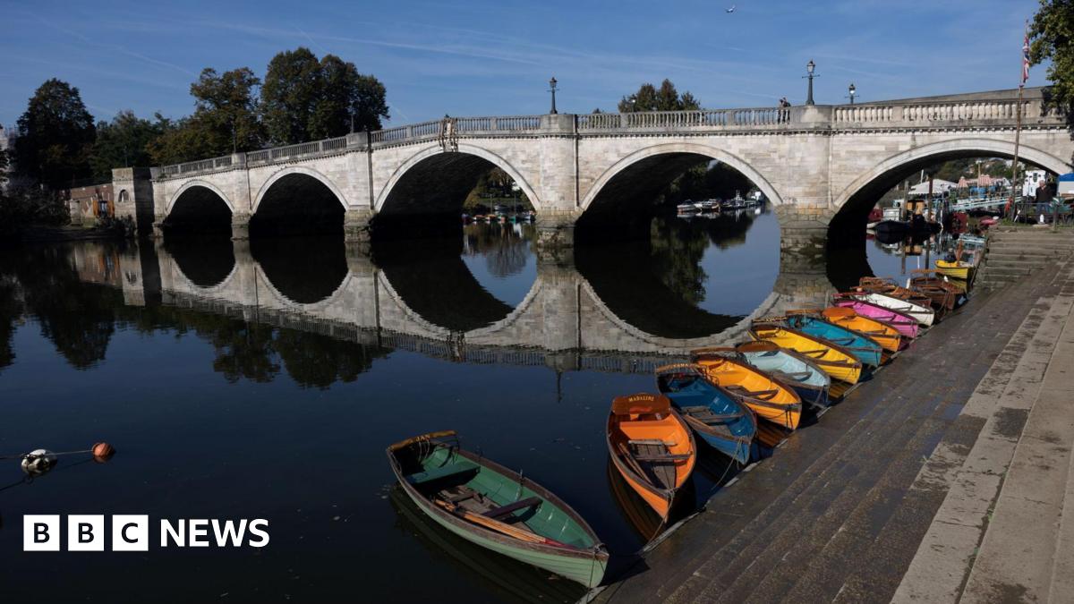 Library image of the Thames at Richmond, on a sunny day. Richmond Bridge is the main focal point of the photograph, with small rowing boats of various bright colours tethered to the concrete steps leading down to the water.