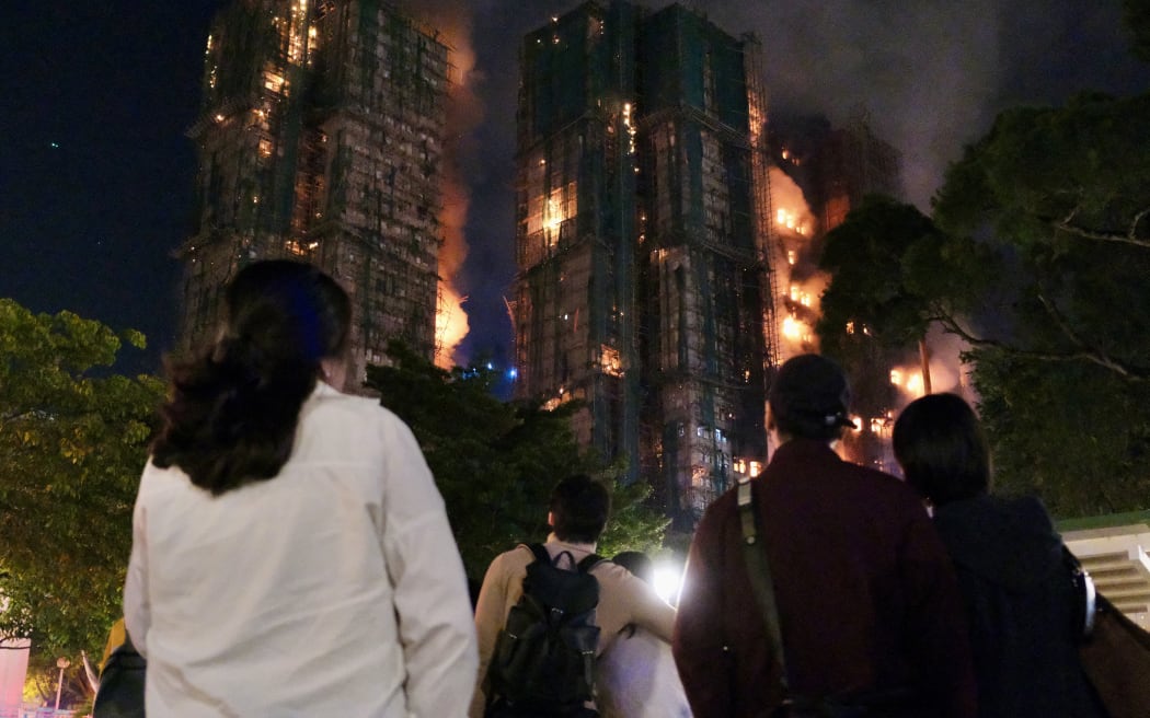 People look on as thick smoke and flames rise during a major fire at the Wang Fuk Court residential estate in Hong Kong's Tai Po district on 26 November, 2025.