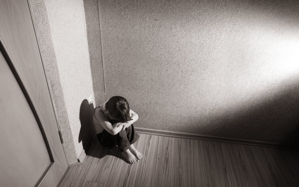 A young boy sits in the corner with his head in his hands (file photo)