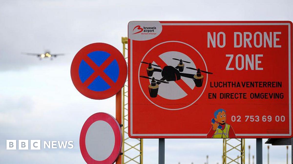Photo shows a sign that reads 'No Drone Zone' near the Brussels-National Airport. A Brussels Airlines passenger jet can be seen coming in to land in the background.